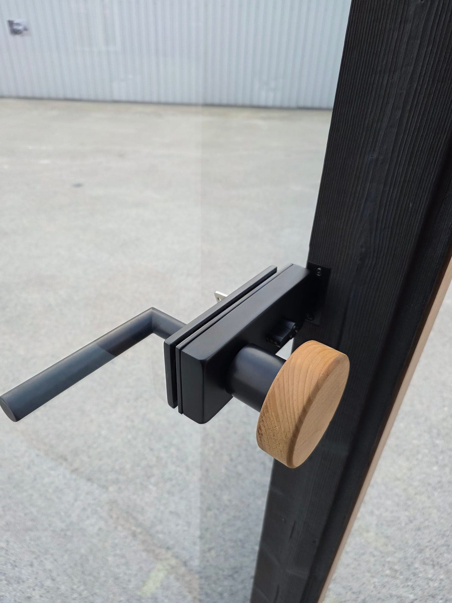 Black handle and wooden turn knob on the glass door of a Wood Architects cube sauna